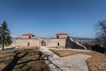 Реставрираната южна порта на крепостта „Цари Мали град“ с две кули с оранжеви покриви и каменна зидария под ясно небе.